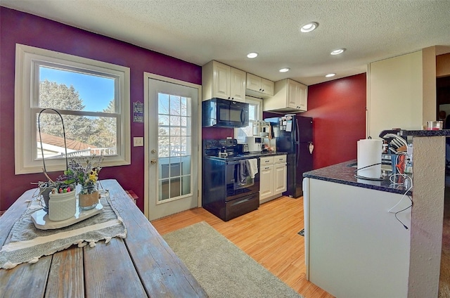 kitchen with black appliances, light wood-style flooring, dark countertops, and a textured ceiling