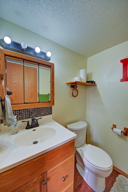 half bath featuring vanity, toilet, and a textured ceiling