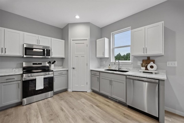 kitchen featuring gray cabinetry, light countertops, light wood-style floors, stainless steel appliances, and a sink