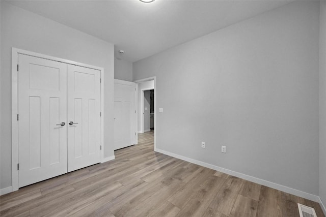 unfurnished bedroom with light wood finished floors, visible vents, a closet, and baseboards