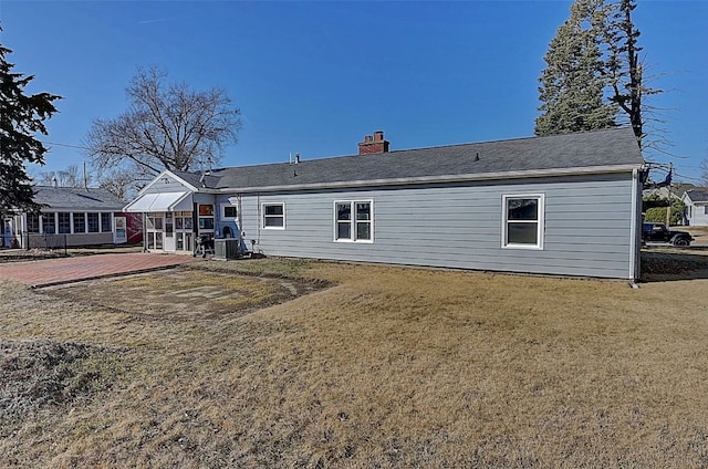 back of property featuring a patio area, central air condition unit, a lawn, and a chimney