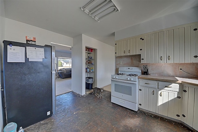 kitchen with white gas range, tasteful backsplash, light countertops, and freestanding refrigerator