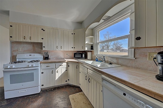 kitchen featuring backsplash, tile counters, cream cabinets, white appliances, and a sink