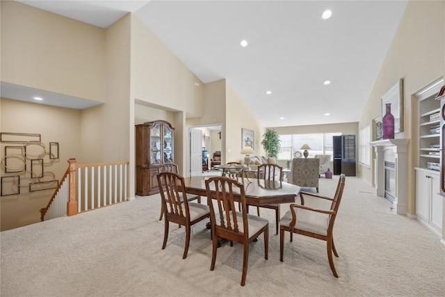 dining space with light carpet, a glass covered fireplace, recessed lighting, and high vaulted ceiling