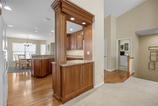 kitchen featuring light stone counters, brown cabinetry, an inviting chandelier, a peninsula, and stainless steel fridge with ice dispenser