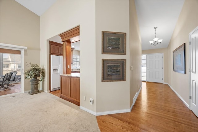 hallway with baseboards, light wood finished floors, high vaulted ceiling, and an inviting chandelier