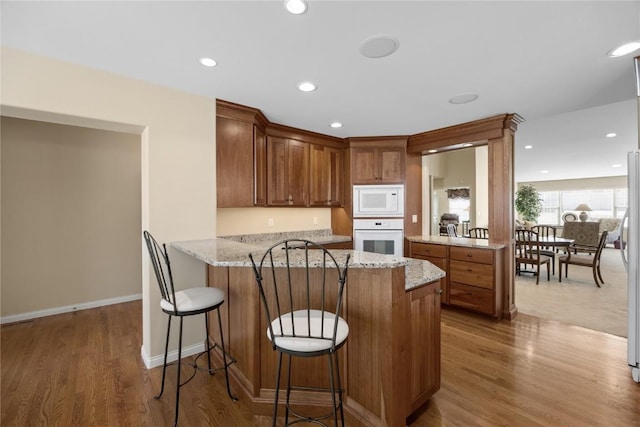 kitchen with white appliances, light stone counters, a peninsula, and wood finished floors