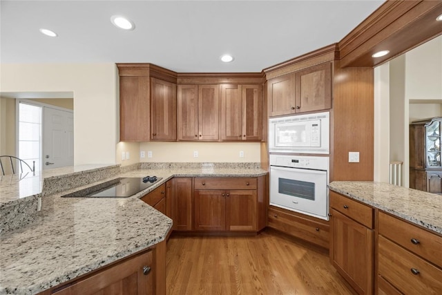 kitchen with white appliances, brown cabinetry, light wood-type flooring, and light stone countertops