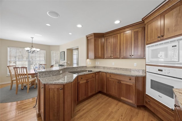 kitchen with white appliances, brown cabinetry, an inviting chandelier, a peninsula, and light wood-style floors