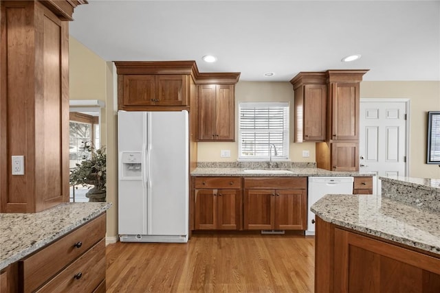 kitchen featuring light wood-type flooring, a sink, recessed lighting, white appliances, and brown cabinetry