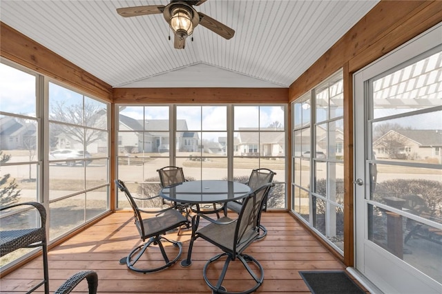 sunroom with lofted ceiling, a ceiling fan, a residential view, and a wealth of natural light