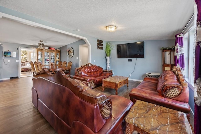 living room with arched walkways, wood finished floors, baseboards, and a textured ceiling