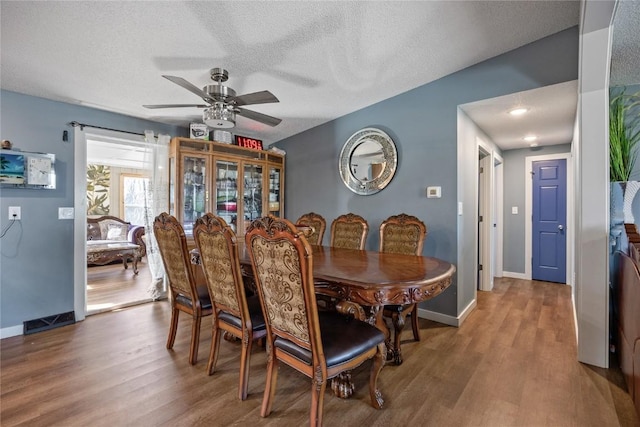 dining space with a textured ceiling, baseboards, a ceiling fan, and wood finished floors