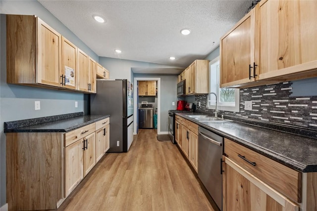 kitchen with a sink, dark countertops, appliances with stainless steel finishes, and light brown cabinetry