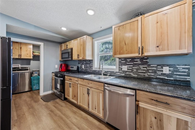 kitchen with a sink, light brown cabinetry, stainless steel appliances, dark countertops, and light wood-type flooring