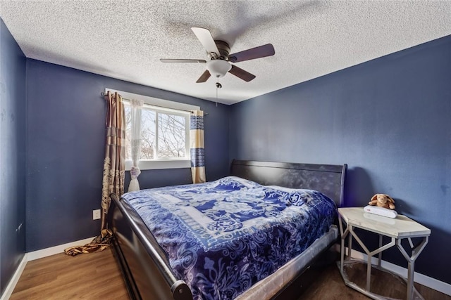 bedroom with a ceiling fan, wood finished floors, baseboards, and a textured ceiling