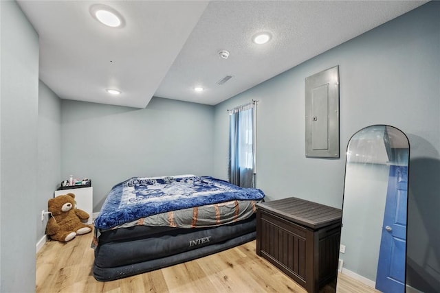 bedroom with electric panel, visible vents, baseboards, and light wood finished floors