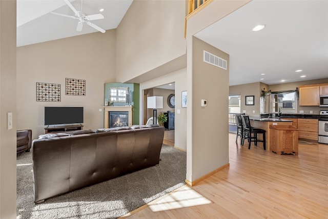 living room with ceiling fan, visible vents, a glass covered fireplace, and light wood-style flooring