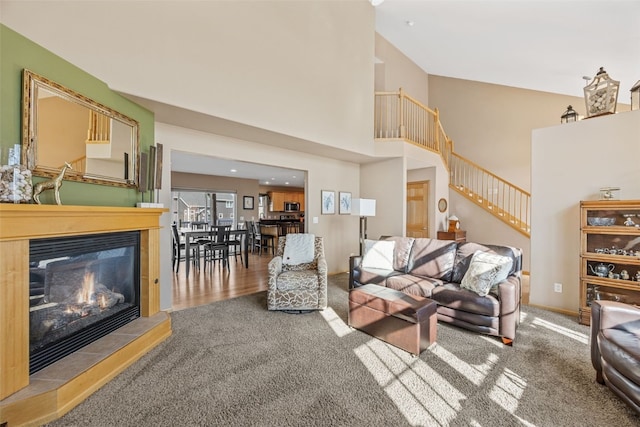 living room with carpet floors, baseboards, a towering ceiling, stairs, and a tile fireplace