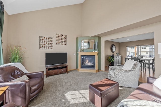 carpeted living area with a glass covered fireplace, a high ceiling, and baseboards