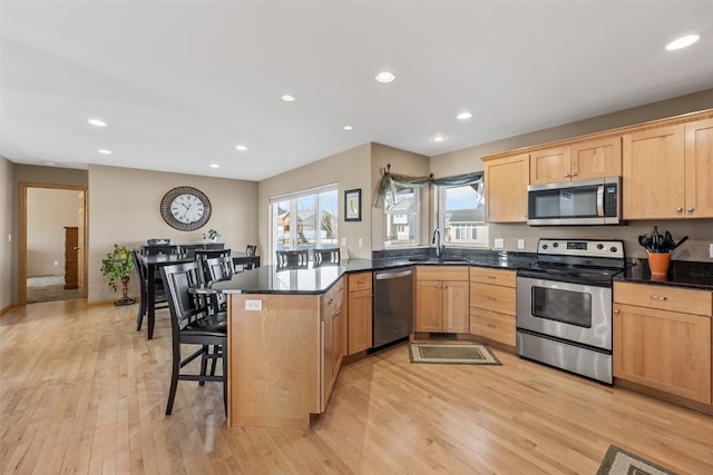 kitchen featuring light brown cabinetry, a peninsula, light wood-style floors, stainless steel appliances, and a sink