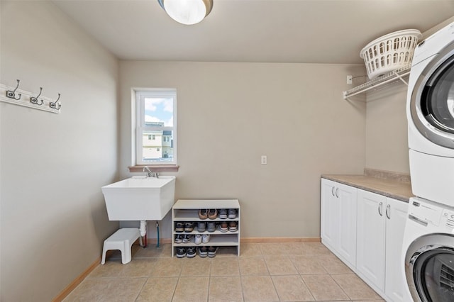 laundry room with light tile patterned floors, stacked washer / dryer, cabinet space, and baseboards