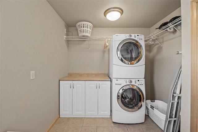 laundry area with light tile patterned floors, cabinet space, baseboards, and stacked washer and dryer