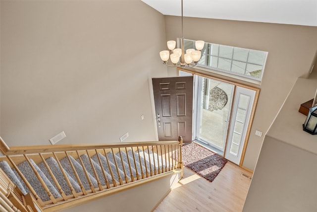 foyer entrance featuring visible vents, a chandelier, stairway, a high ceiling, and wood finished floors