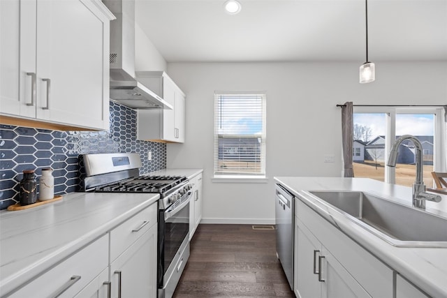 kitchen featuring tasteful backsplash, a sink, wall chimney range hood, appliances with stainless steel finishes, and dark wood-style flooring