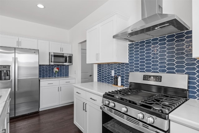 kitchen with dark wood finished floors, stainless steel appliances, white cabinets, wall chimney range hood, and decorative backsplash