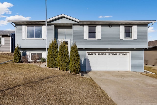 raised ranch with concrete driveway, a garage, and a front lawn