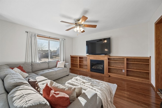 living room with wood finished floors, a glass covered fireplace, and a ceiling fan