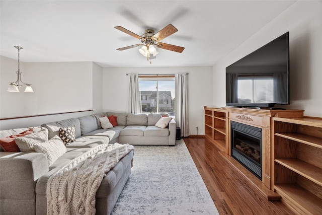 living area featuring a glass covered fireplace, ceiling fan, and wood finished floors