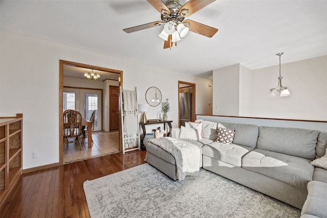 living area with baseboards, dark wood finished floors, and ceiling fan with notable chandelier