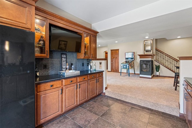 kitchen with tasteful backsplash, dark countertops, dark carpet, brown cabinetry, and glass insert cabinets