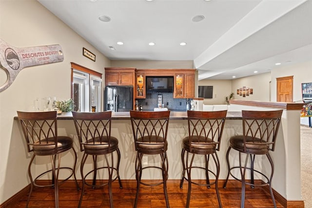 kitchen with a kitchen bar, dark wood-type flooring, backsplash, and black fridge