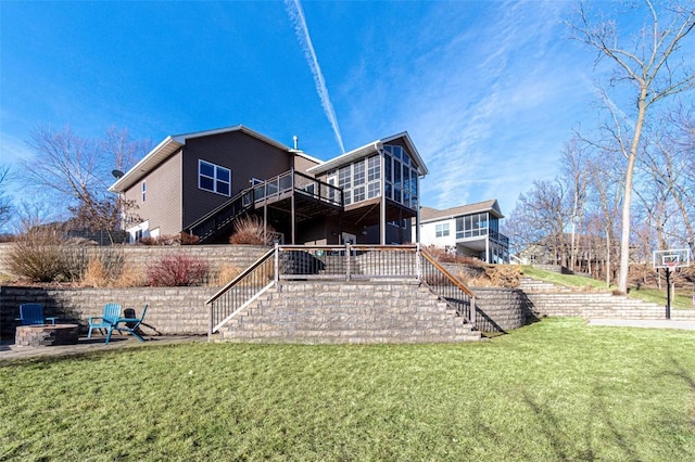 rear view of house featuring stairway, a wooden deck, a yard, a sunroom, and a fire pit