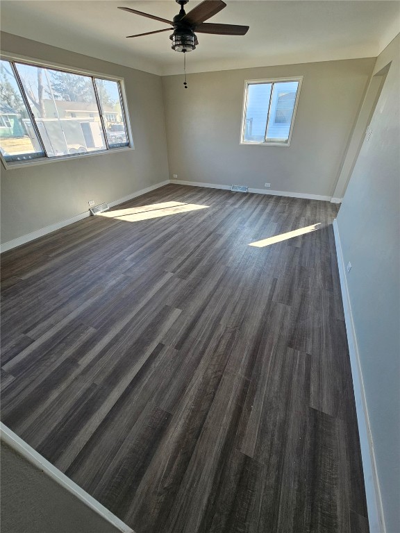 unfurnished room with visible vents, baseboards, dark wood-type flooring, and ceiling fan