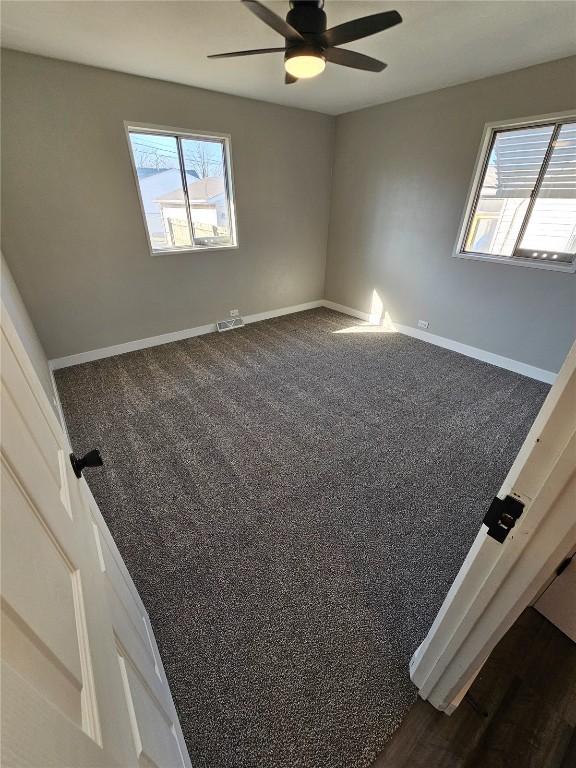 unfurnished room with a ceiling fan, baseboards, and dark colored carpet