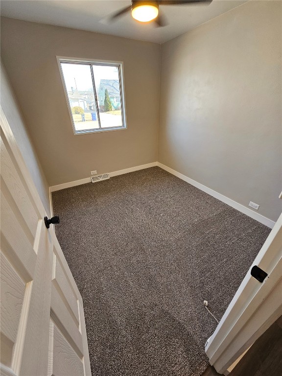 carpeted spare room with visible vents, baseboards, and a ceiling fan