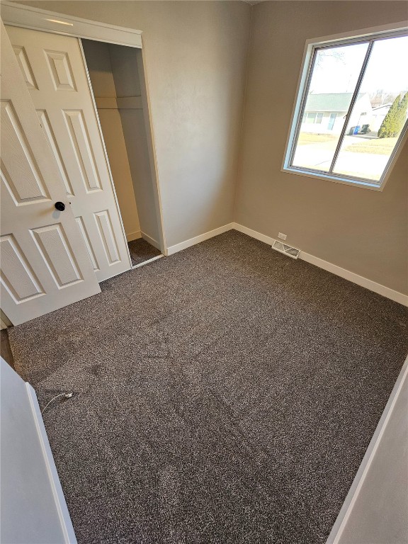 unfurnished bedroom featuring a closet, baseboards, visible vents, and dark carpet