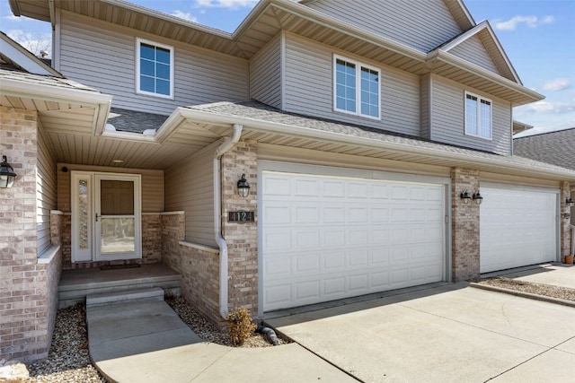 doorway to property with concrete driveway, an attached garage, brick siding, and a shingled roof