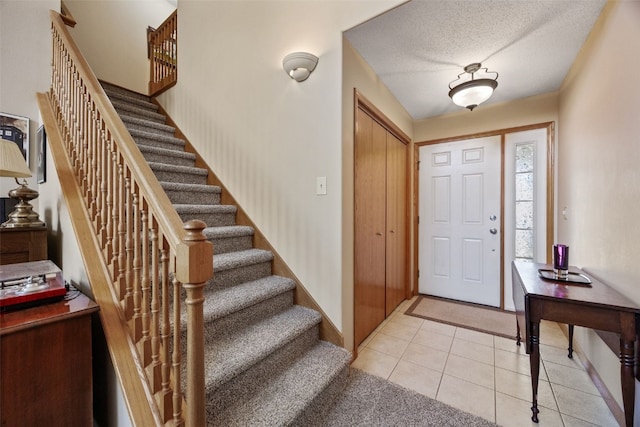 entryway featuring light tile patterned floors, baseboards, a textured ceiling, and stairs