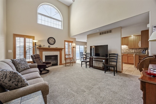 living area featuring a tiled fireplace, light tile patterned floors, visible vents, and light carpet