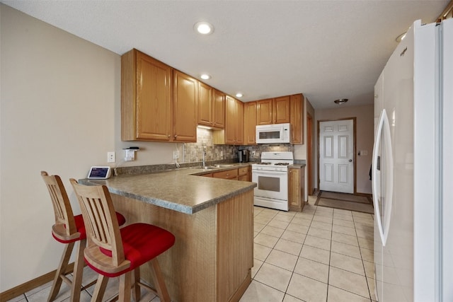 kitchen featuring backsplash, a breakfast bar area, light tile patterned floors, a peninsula, and white appliances