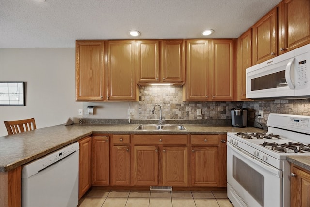 kitchen featuring white appliances, visible vents, a peninsula, a sink, and brown cabinets