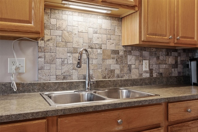 kitchen with dark countertops, backsplash, brown cabinetry, and a sink