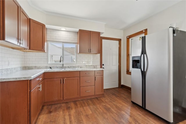 kitchen featuring tasteful backsplash, light countertops, wood finished floors, stainless steel fridge, and a sink