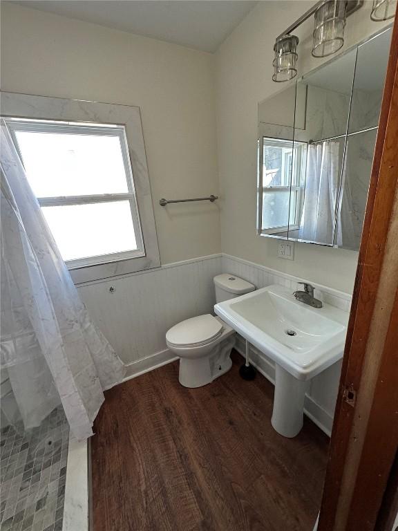 bathroom with a wainscoted wall, curtained shower, toilet, and wood finished floors