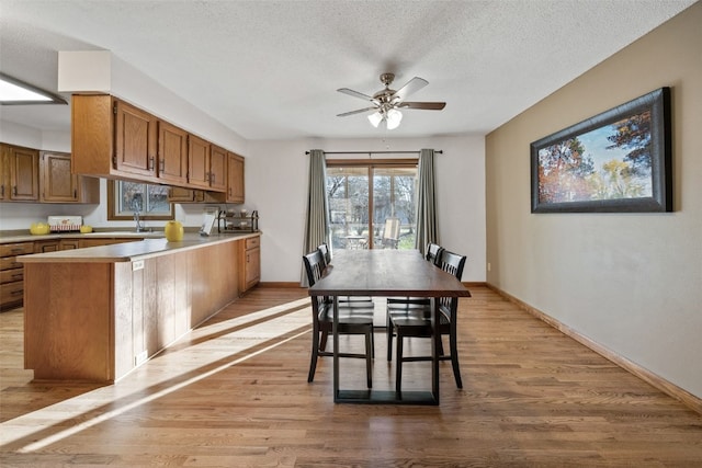 dining room with light wood-style flooring, a ceiling fan, baseboards, and a textured ceiling